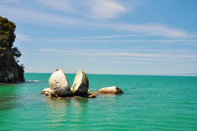Split Apple Rock - a curious rock formation in Abel Tasman National Park. The rounded sphere boulder is set off-shore in the ocean and is perfectly slit in half. The 2 halves are separated like 2 wedges propped against each other. The rock is surrounded by beautiful turquoise water.