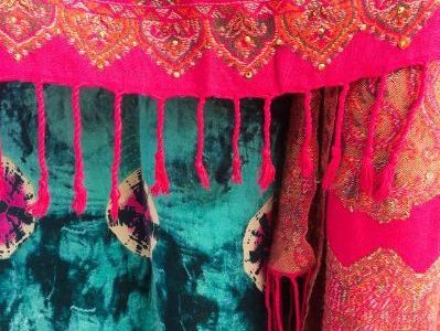 The beautiful and brightly coloured cloth of an Indian sari. Pink with gold and crimson embroidery overlaying a skirt tie died blues, pinks and indigo.
